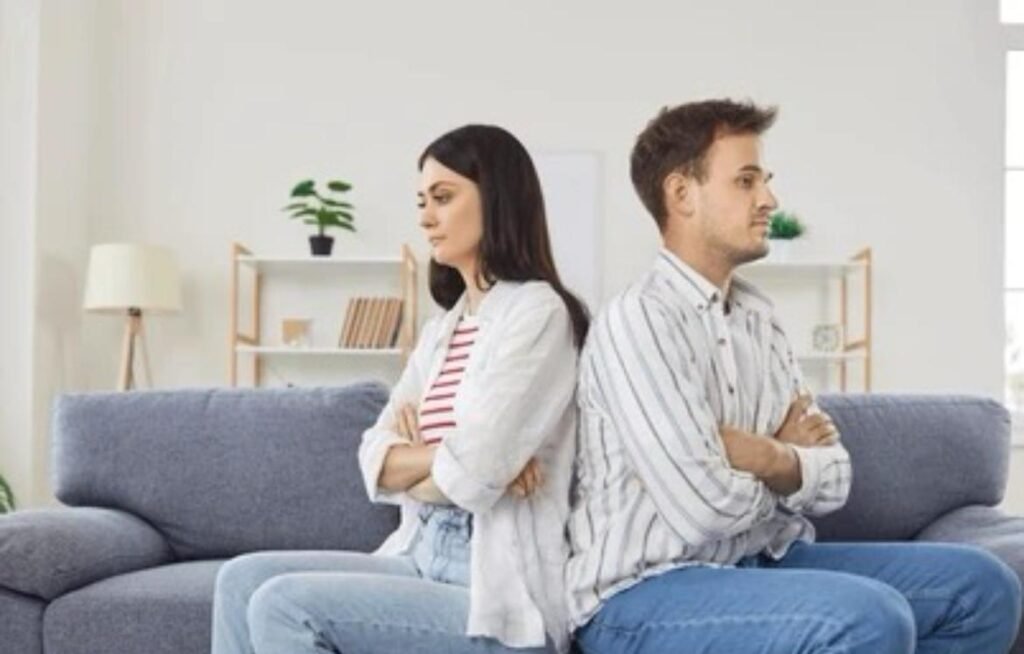 Pareja sentada de espaldas con los brazos cruzados, mostrando distancia emocional y conflicto típico de relaciones que agotan o dependencia emocional.
